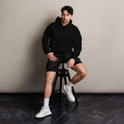 Reservoir Classics Unisex Men and Womens hoodie in black with no drawstring. A vintage, classic vibe streetwear style clothing line.  Man sitting on stool to model